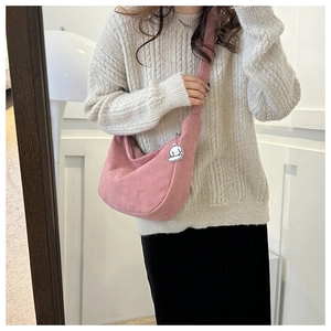 Pink corduroy crossbody bag with cute plush pendant shown on woman in cream sweater