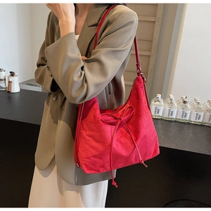 Detail of a red suede tote bag with drawstring closure worn by a model in a blazer