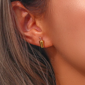 Close-up of a gold beverage cup earring with pink gems worn on an earlobe
