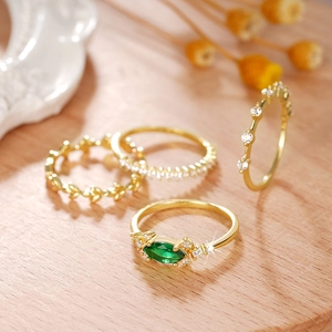 Detalle de set de cuatro anillos apilables dorados con esmeralda y circón sobre madera