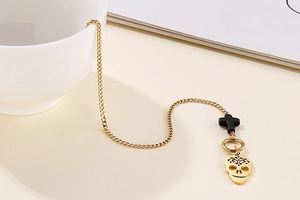 Macro detail of gold curb chain with black cross and hollow skull pendant charms