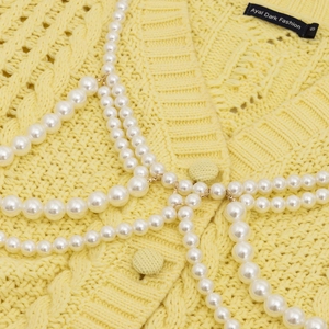 Close-up of multilayer pearl body chain worn over yellow cardigan beach jewelry