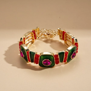 Détail de la chaîne vintage dorée avec émail vert, perles rouges et gemmes roses sur fond beige