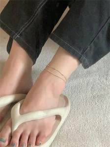 Detail of a minimalist gold double-layer snake chain anklet with small beads on a model