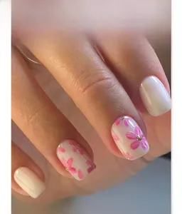Detail of short square press-on nails featuring pink floral patterns and gold beads
