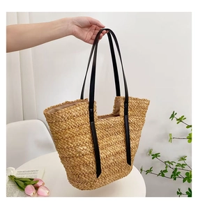 Détail du sac cabas en paille tressée avec de longues anses en cuir noir contrasté