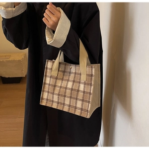 Detail of checkered canvas tote bag with beige handles held by a model in casual wear