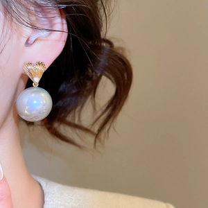 Close-up of golden textured heart stud earring with large iridescent pearl on model