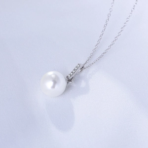 Macro shot of s925 silver pearl necklace featuring a zircon pendant on white silk fabric