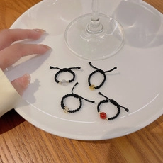 Detail of four handmade braided rope rings with colorful beads in a white ceramic dish