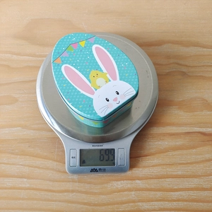 Flat Easter egg-shaped tin box with rabbit illustration weighing 69.9g on scale
