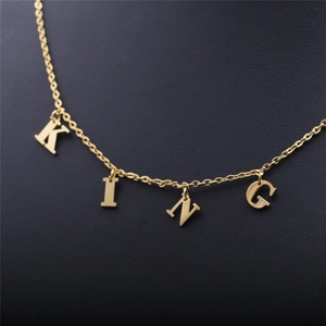 Close-up of golden stainless steel KING letter pendants on a textured dark background