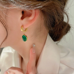 Gros plan d'une boucle d'oreille vintage en résine émeraude sur l'oreille dorée