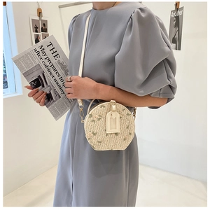 Detail of round straw crossbody bag featuring floral embroidery and PU leather strap