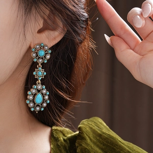 Close-up of vintage floral drop earrings with turquoise stones and white beads on model