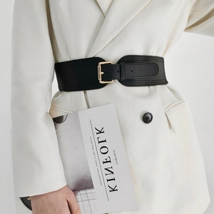 Detail of a black wide elastic waist belt with a gold rectangular buckle on a white blazer