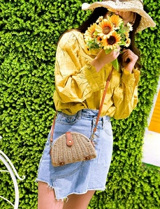 Detail of a mini semi-circle straw crossbody bag with brown leather flap and button