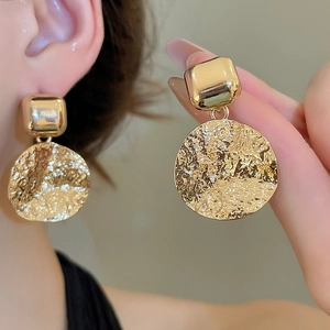 Detail of gold square and hammered round drop earrings worn by a model