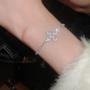 Detail of a silver chain bracelet featuring a pink zircon flower cross pendant on a wrist