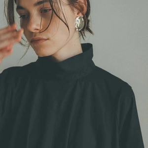 Close-up of a silver oversized geometric oval metal earring worn with a black turtleneck