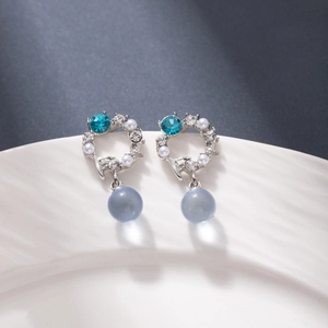 Elegant geometric silver earrings with blue crystals and white pearls on ceramic tray