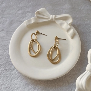 Matte gold double irregular oval hoop earrings on white porcelain decorative tray