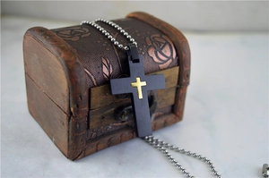 Close-up of black and gold cross pendant with brushed metal texture and bead chain
