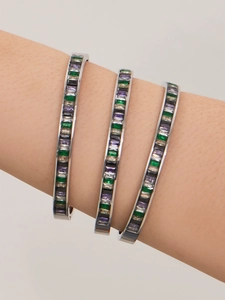 Close-up of three stacked silver bracelets with emerald, purple, and black zircon stones