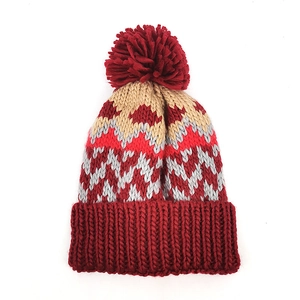 Colorful zigzag knit beanie with a large red pompom and thick folded cuff for winter