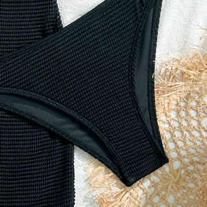 Close-up of black waffle textured swimsuit fabric on a woven straw mat decoration