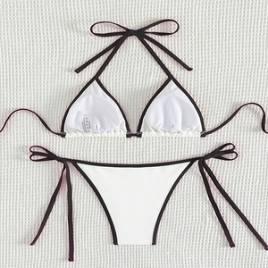 Two-piece white bikini set with black contrast trim and side-tie bottoms on textured fabric