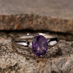 Macro shot of an oval purple amethyst ring on a natural rock to show the silver metal detail