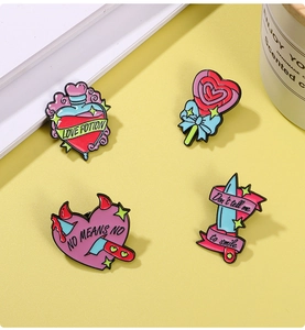 Detail of four enamel pins with heart, dagger, and candy designs on a yellow background