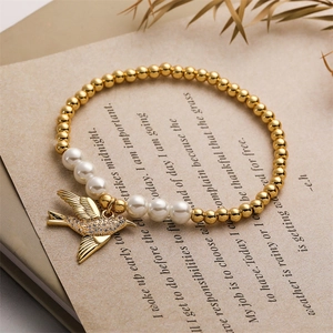 Détail du bracelet perlé avec pendentif oiseau doré et perles blanches sur livre