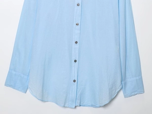 Detail of light blue linen shirt featuring dark buttons and a curved hemline