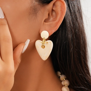 Detail of model wearing gold drop earrings with heart-shaped marbled resin pendants