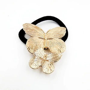 Detailed close-up of golden alloy butterfly hair tie with sleek black elastic band