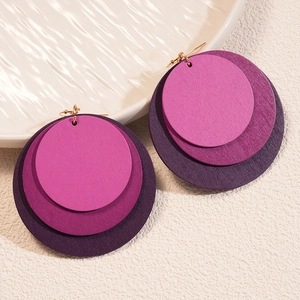 Detail of layered purple geometric wooden hoop earrings on a textured white surface