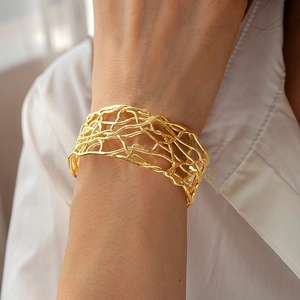 Macro shot of an 18K gold-plated mesh intertwined open cuff bracelet on a model
