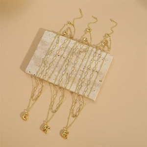 Gold layered initial necklaces with G, H, E pendants on elegant beige marble display