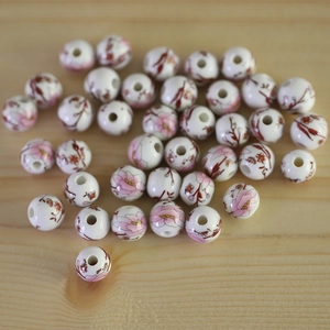 Round ceramic flower beads with pink floral patterns on natural wood background