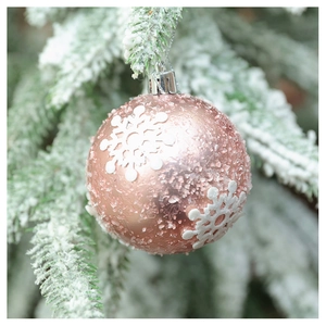 Detail of rose gold Christmas ball with white snowflake texture on snowy pine branch