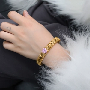 Detail of gold woven leaf bracelet with a pink heart gemstone on a model's wrist