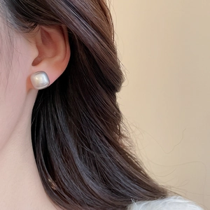Close-up of square geometric stud earrings showing pearlescent texture and elegant fit