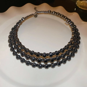 Detail of a multi-layer black rhinestone choker necklace placed on a white porcelain dish