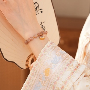 Detailed close-up of pink sunstone beaded bracelet with a golden rocking horse charm