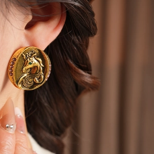 Macro shot of vintage gold unicorn earrings with purple rhinestones and green gem inlay