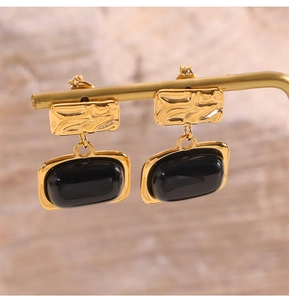 Detail of vintage square gold-plated earrings with black glass on a jewelry stand