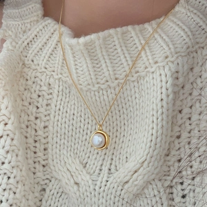 Close-up of a minimalist round pearl necklace with golden frame on a beige sweater
