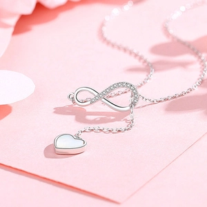 Detail of silver Y-necklace featuring a crystal infinity symbol and heart pendant